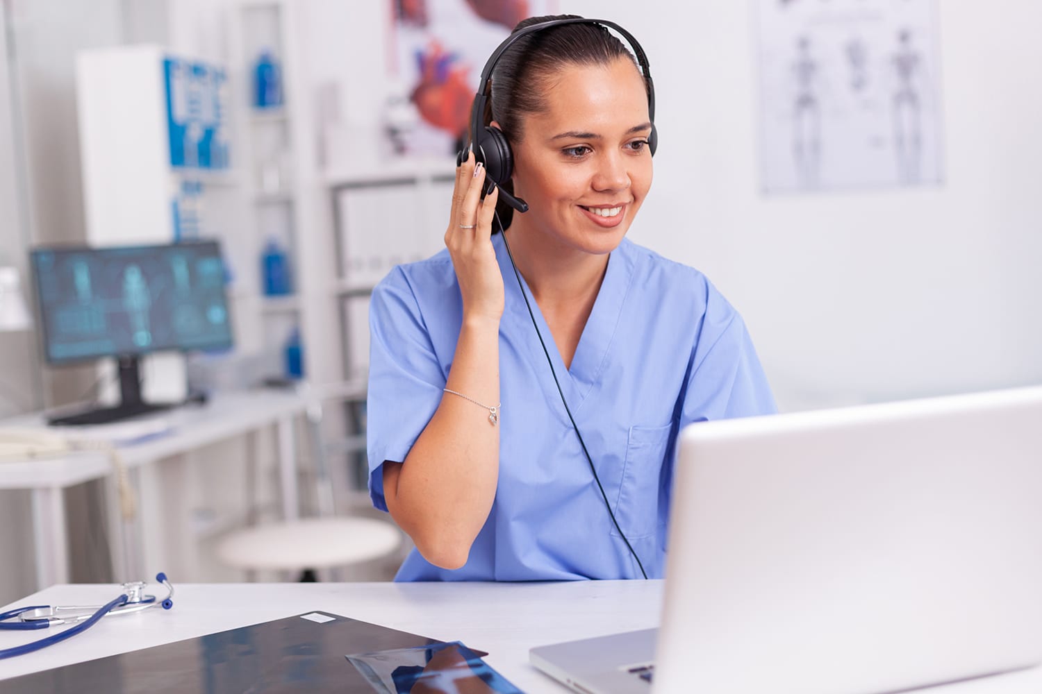 Medical staff talking with patient about prescription wearing headset with microphone in hospital office. Health care physician sitting at desk using computer in modern clinic looking at monitor.
